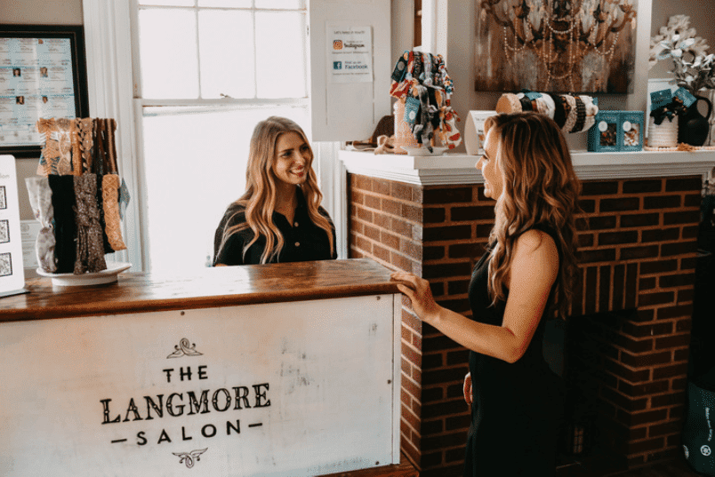 Two women conversing at the reception of The Langmore Salon, with hair accessories on display.