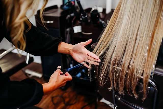 Person cutting long blonde hair in a salon.