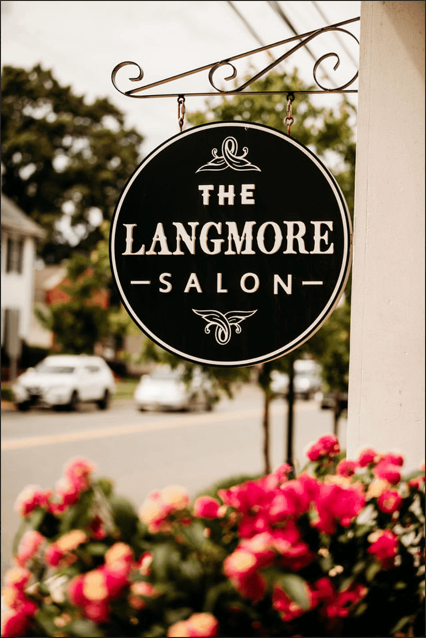 The Langmore Salon sign with pink flowers and a street in the background.